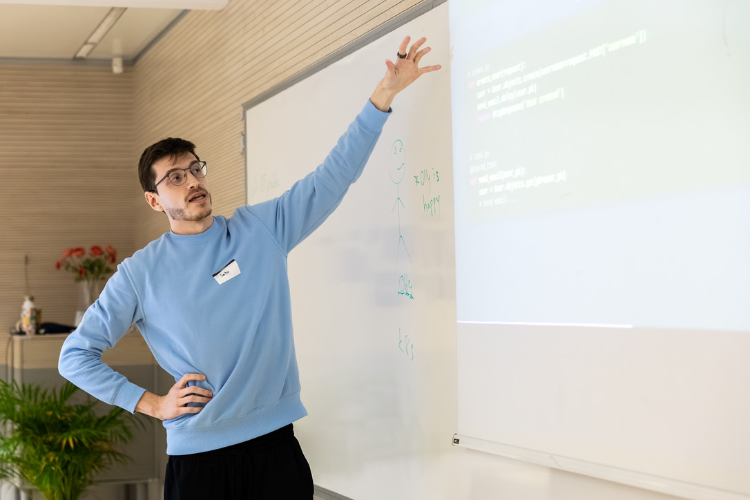 Predavatelj v modrem puloverju kaže proti projekciji.